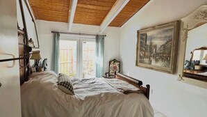 A bedroom with a bed, a wooden ceiling, a window with curtains, a painting on the wall, and a mirror. - Hemingway Inspired Villa (Sarasota)