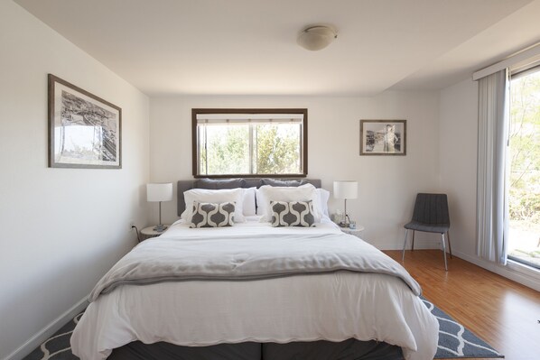 A bedroom with a large bed, two bedside tables, a chair, and a window with a view of trees.