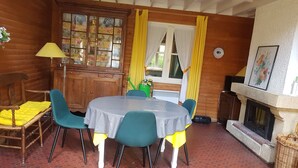 A cozy room with a wooden interior, a round table with chairs, a cabinet with glass doors, a fireplace, and a window with curtains. - House (Condette)