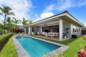 Ein modernes Haus mit Swimmingpool, überdachter Terrasse und Gartenmöbeln.