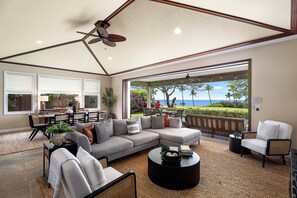 Ein großzügiges Wohnzimmer mit einer breiten Couch, einem runden Couchtisch und Blick aufs Meer.