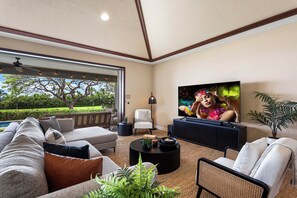 Ein geräumiges Wohnzimmer mit einem großen Fernseher, bequemen Sitzgelegenheiten und Blick ins Freie.