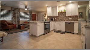 Une cuisine moderne avec des meubles blancs, un îlot central et un coin repas comprenant un canapé et un fauteuil.