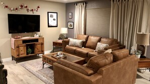 Un salon avec un canapé en cuir marron, un meuble de rangement en bois, un téléviseur à écran plat et un tapis à motifs.