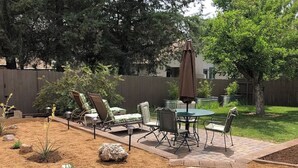 Une terrasse avec une table et des chaises, entourée d’un jardin agrémenté de rochers et de plantes.