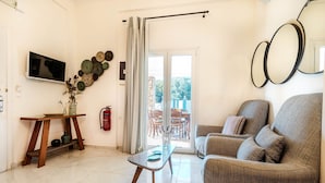 A living room with a sofa, a TV, a table, and a view to the outside. - Villa Sun Sole (Corfu)