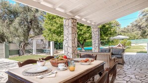 An outdoor patio with a table set for breakfast, surrounded by stone pillars and a pool in the background. - Villa Sun Sole (Corfu)