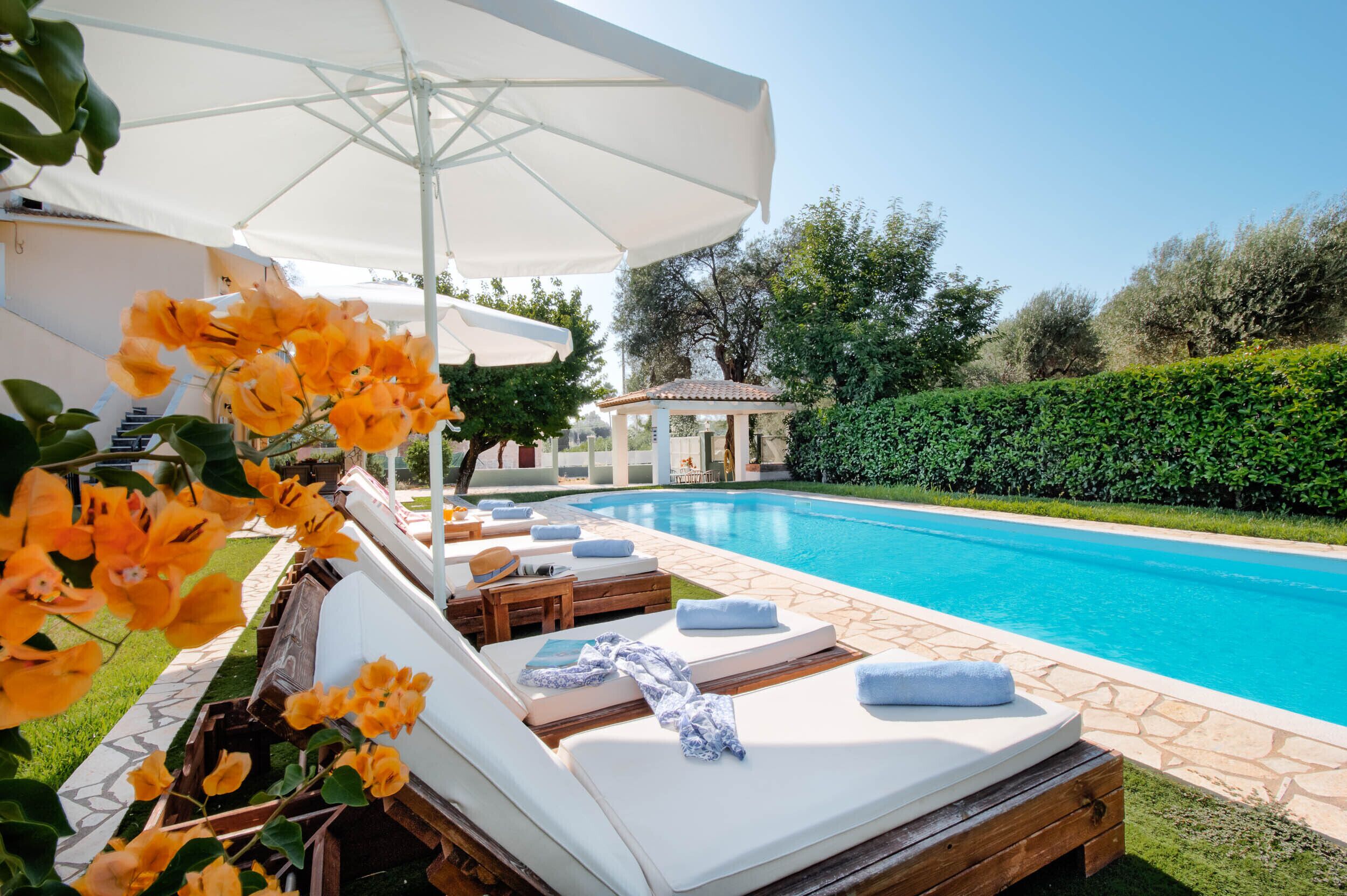 A poolside area with lounge chairs, a pergola with an umbrella, and a gazebo in the background.