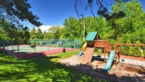A playground with a slide, climbing structure, and a tennis court. - Spacious 2 Bdrm Condo Walking distance to Weirs Beach!! (Laconia)
