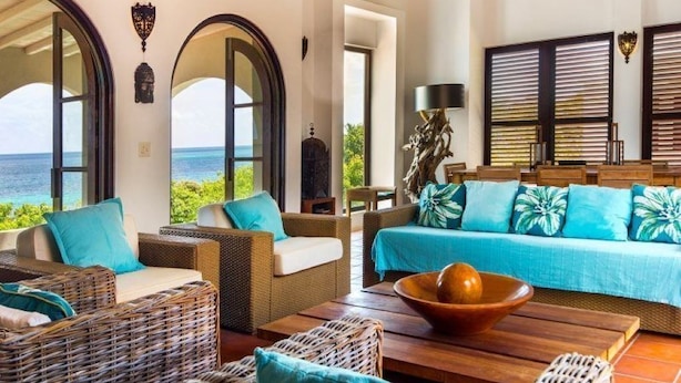 Amplia sala de estar con muebles de mimbre, una mesa de centro de madera y vista al océano.