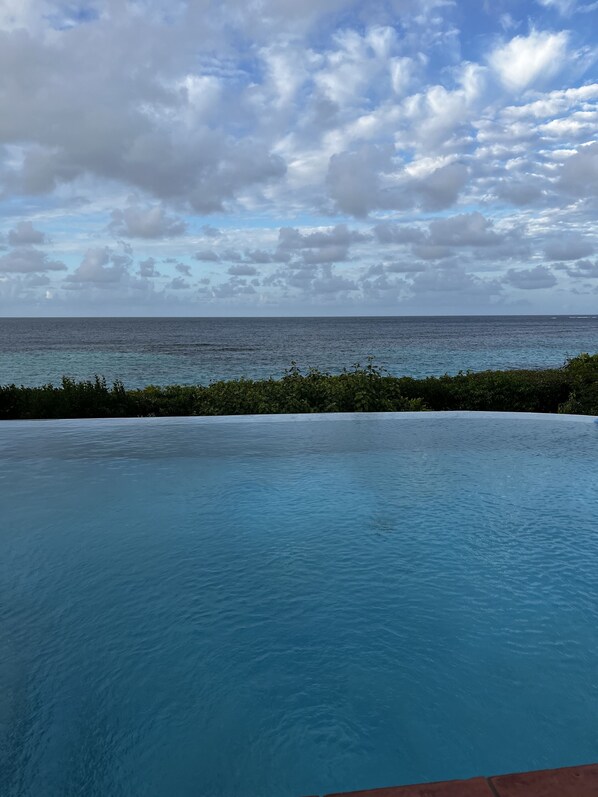 A view of a swimming pool with a view of the ocean and a cloudy sky.