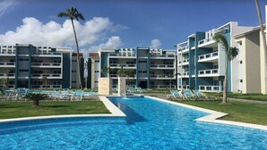 Ein Hotel mit zentralem Schwimmbecken, mehreren Balkonen und wolkenlosem Himmel.