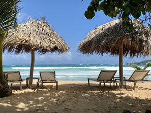 A beach with thatched umbrellas and lounge chairs facing the ocean.