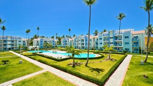 Ein Resort mit mehreren Gebäuden in Blau und Weiß, einem zentral gelegenen Swimmingpool und gepflegten Palmen.