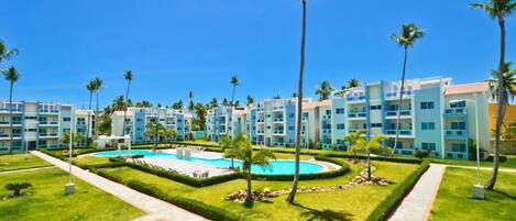 A resort with multiple blue and white buildings, a central swimming pool, and well-maintained palm trees.