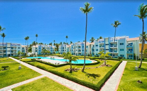 A resort with multiple blue and white buildings, a central swimming pool, and well-maintained palm trees.