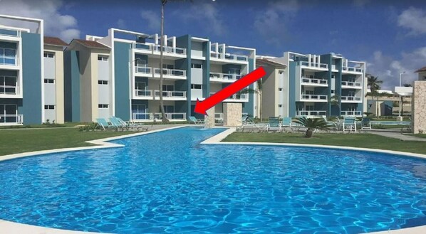 A modern hotel with a central swimming pool, multiple balconies, and a clear sky.