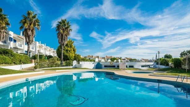 Une piscine d’un bleu éclatant, entourée de bâtiments blancs et de palmiers, sous un ciel d’un bleu profond.