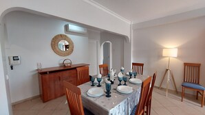 Un coin repas avec une table dressée pour six personnes, des chaises en bois, un buffet, un climatiseur fixé au mur, un miroir et une lampe sur pied.