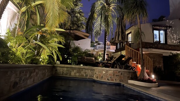 A pool area with a stone wall, palm trees, and a building with a balcony.