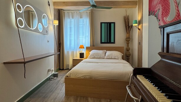 Habitación de hotel con cama, ventilador de techo, piano y espejo con luces.