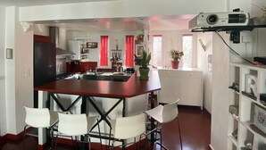 Una cocina moderna con una isla central, sillas blancas y un proyector montado en la pared.
