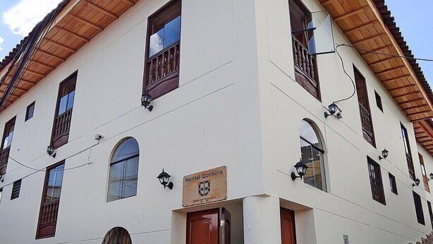 A two-story building with a white facade, wooden roof, and a sign indicating it is a hostel. - Qorikilla Hostal (Cusco)