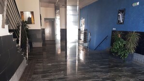 A hallway with a polished stone floor, a staircase on the left, and a blue wall with a poster on the right. - Oropesa Ciudad de Vacaciones 3000 (Oropesa del Mar)