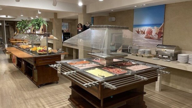 Un área de buffet con varias estaciones de comida, una máquina de café y un cartel grande en la pared.