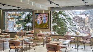 A restaurant with round tables and chairs, large windows with a snowy view, and a painting on the wall. - NH Collection Andorra Palome (Arinsal)