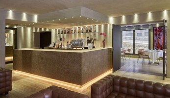 Un bar moderno con barra central, zona de estar con sofás de cuero y vistas al exterior a través de amplios ventanales.