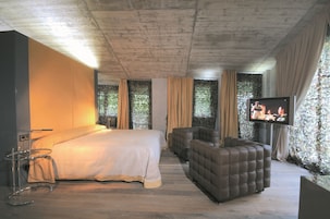 Una habitación de hotel moderna con una cama grande, un sofá, un televisor y una mesita.