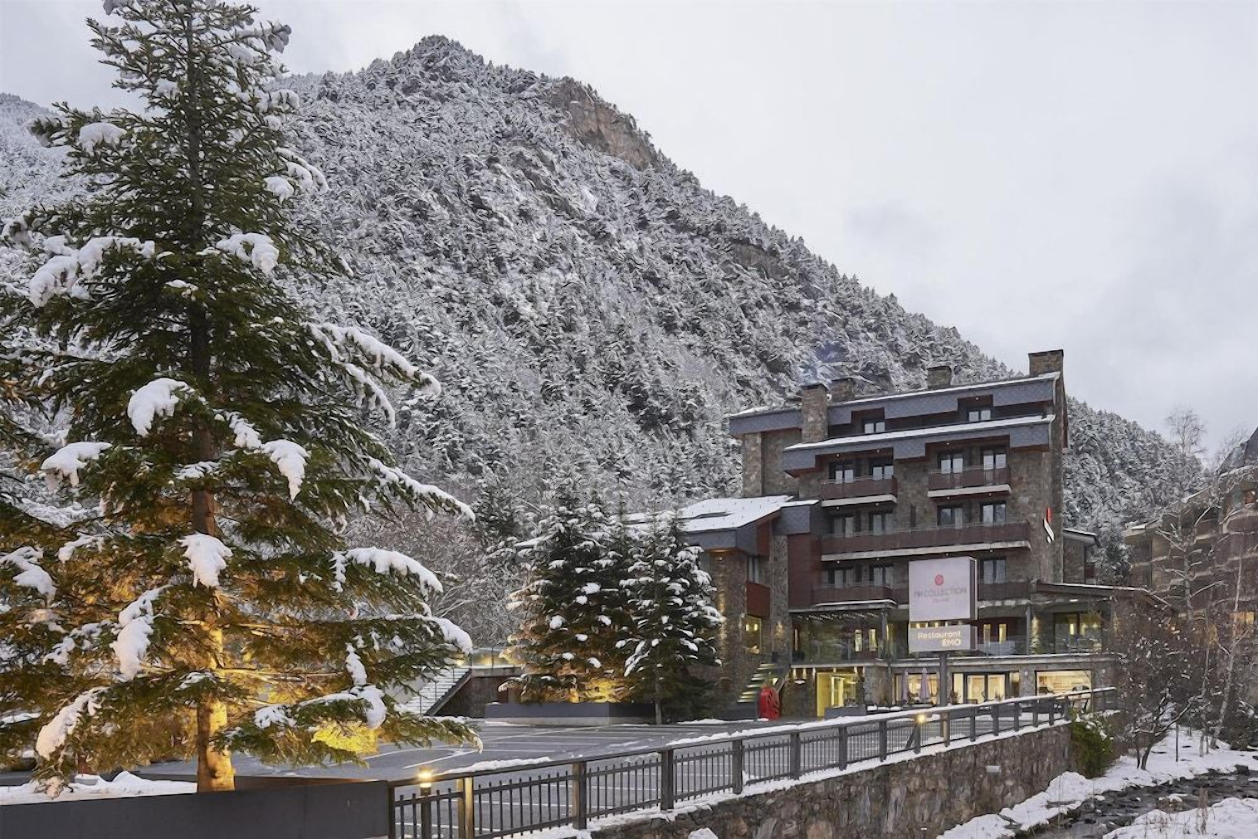 A hotel with a mountain backdrop, featuring a multi-story building with balconies and a restaurant sign.