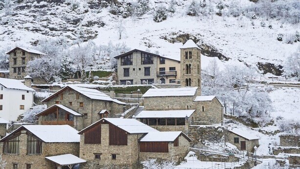 Un pueblo cubierto de nieve con edificios de piedra, incluyendo una torre destacada.