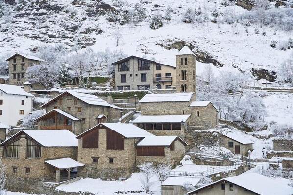 A snow-covered village with stone buildings, including a prominent tower. - NH Collection Andorra Palome (Arinsal)