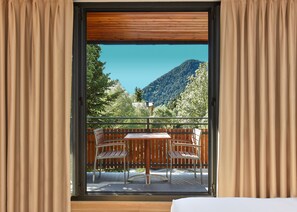 Ein Zimmer mit einem Balkon, der einen Holztisch und Stühle, einen Blick auf einen Berg und Vorhänge an den Fenstern bietet.