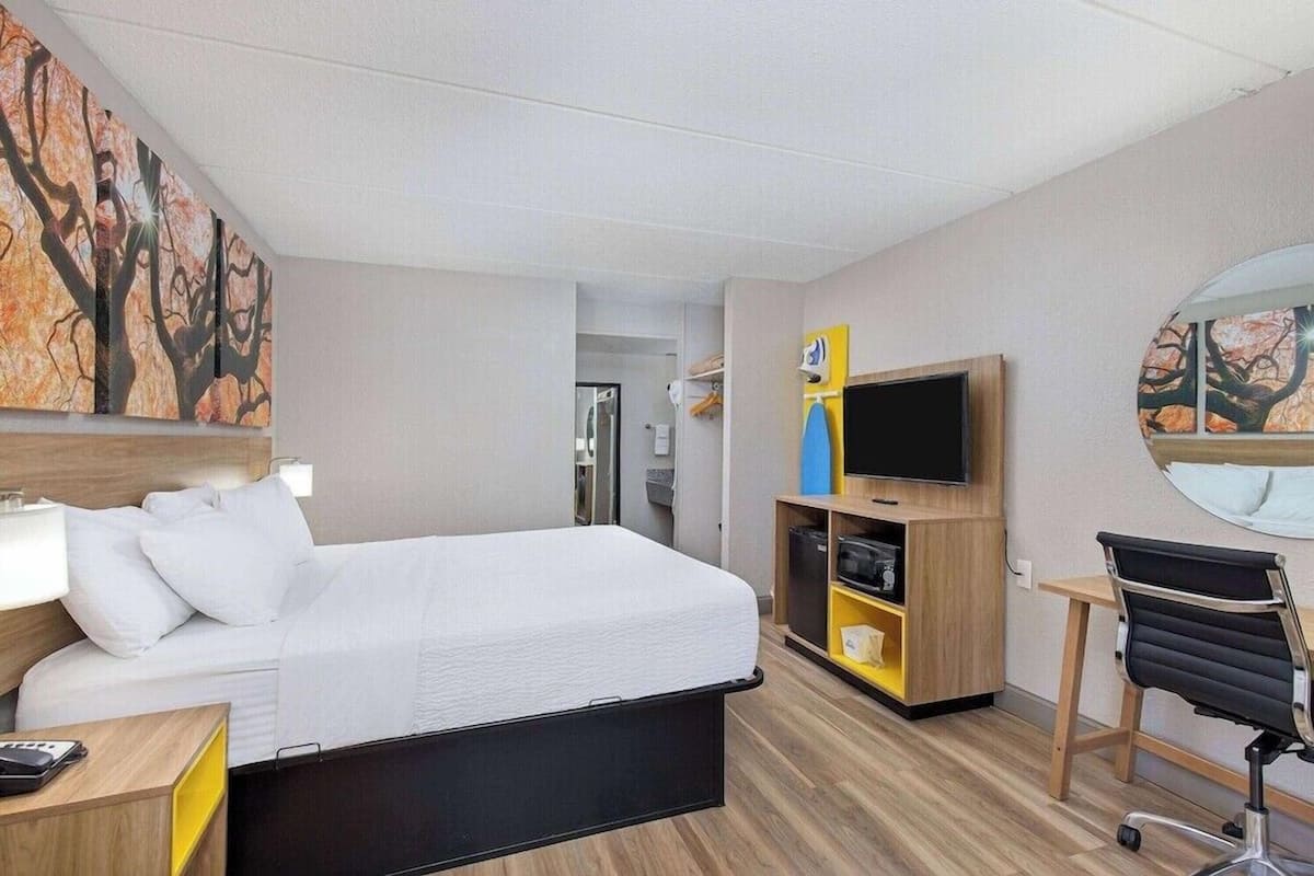 A hotel room with a bed, a desk, a chair, a TV, and artwork on the walls.