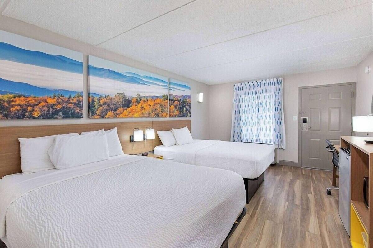 A hotel room with two beds, a painting of autumn foliage, a patterned curtain, and a door.