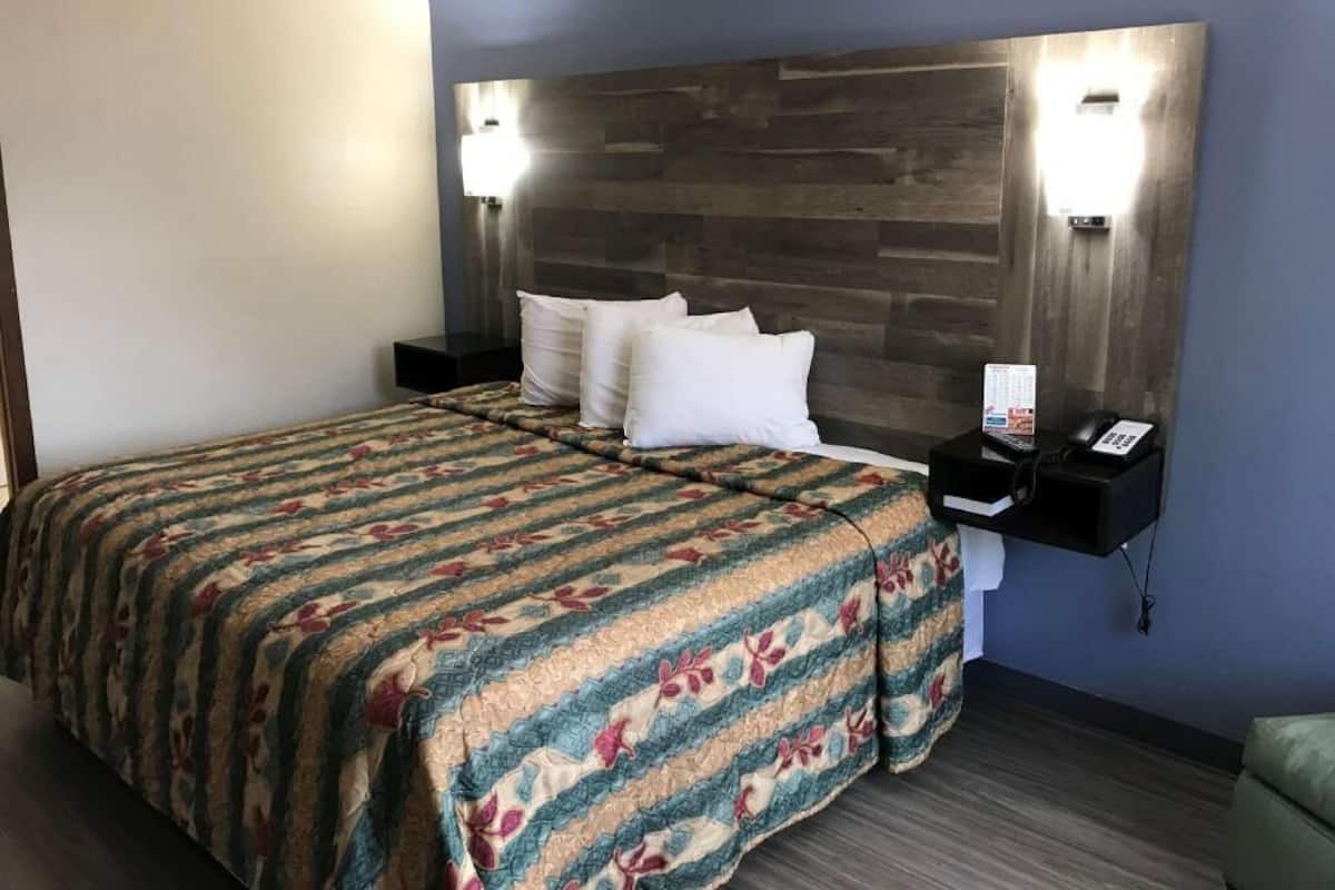A hotel room with a bed, a nightstand with a phone, and a wall-mounted light fixture.