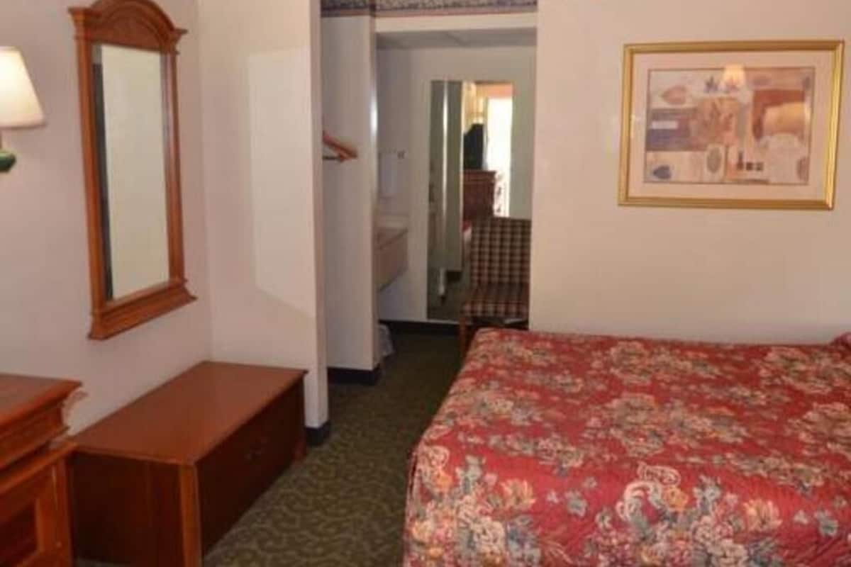 A hotel room with a bed, a dresser, a mirror, and a framed picture on the wall.