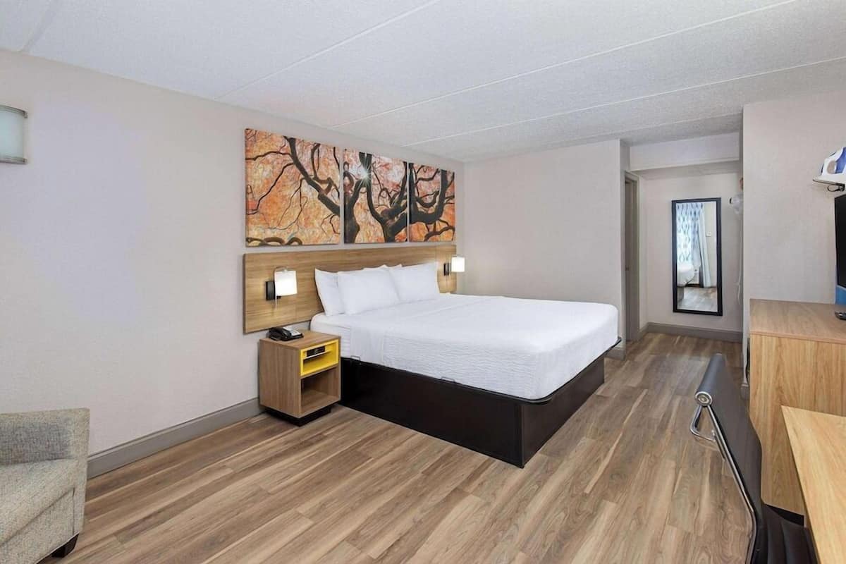 A modern hotel room with a large bed, wooden flooring, a desk, and a painting on the wall.