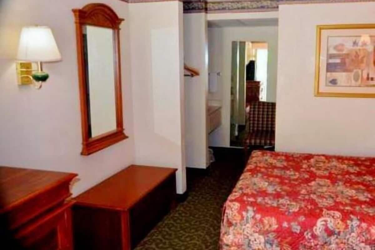 A hotel room with a bed, a bedside table, a mirror, a lamp, and a framed picture on the wall.