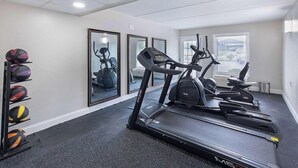 Un gimnasio con cintas de correr, elípticas y un estante de balones deportivos.