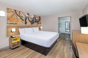 A hotel room with a bed, bedside tables, artwork on the wall, a TV, and a door leading to a bathroom. - Days Inn By Wyndham Knoxville North (Knoxville)