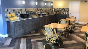 Una cocina moderna con una isla integrada, armarios oscuros y un salpicadero estampado. Cuatro sillas de mimbre rodean una mesa de madera.