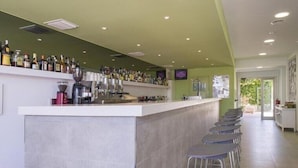 A modern bar area with a long counter and multiple stools, a tiled floor, and a green accent wall. - Hotel Bahia Playa (Sant Josep de sa Talaia)