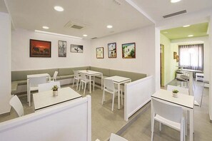Moderni hotellihuone, jossa on oleskelualue, valkoiset huonekalut ja taideteoksia seinillä.