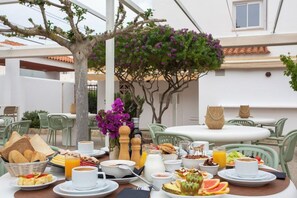 An outdoor dining area with a table set for breakfast, including bread, eggs, and fruit. - Hotel Bahia Playa (Sant Josep de sa Talaia)