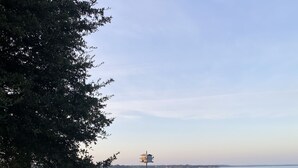 Vista al frente del agua con un pabellón, una pequeña torre y un muelle que se adentra en el agua.