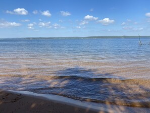 Una playa con agua cristalina, una orilla arenosa y una costa distante con edificios.
